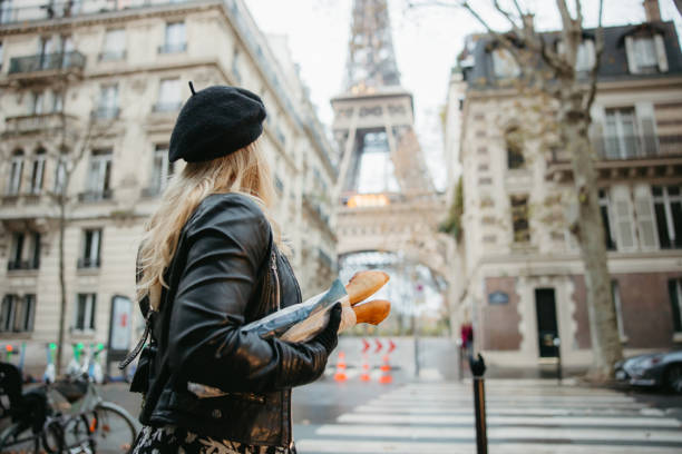 woman with blond hair, standing at a crosswalk, carrying two baguettes, eiffel tower, paris in background - food stock pictures, royalty-free photos & images