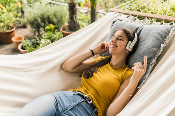 woman with eyes closed listening music through headphones while relaxing on hammock in yard - garden decoration photos et images de collection