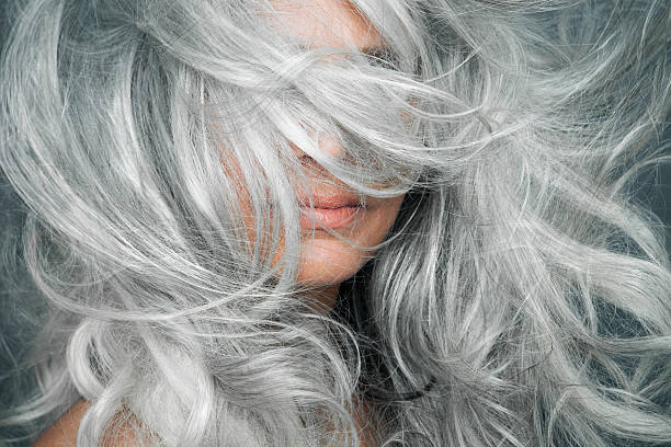 woman with grey hair blowing across her face. - hairstyle stock-fotos und bilder