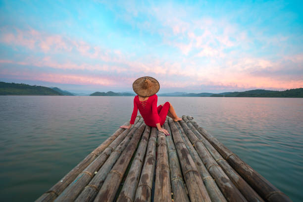 woman with red dress and traditional hat sitting on a wooden raft - travel stock pictures, royalty-free photos & images