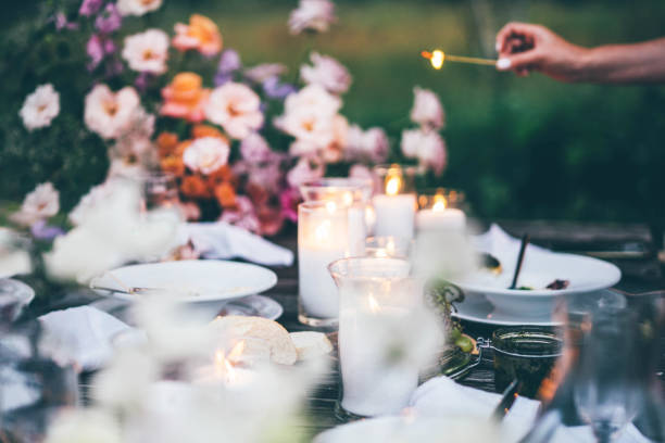 women ignite fire to decorative candles in stylish glass holders with thin wooden sticks at rustic table with elegant setting in garden closeup. - garden decoration stock pictures, royalty-free photos & images