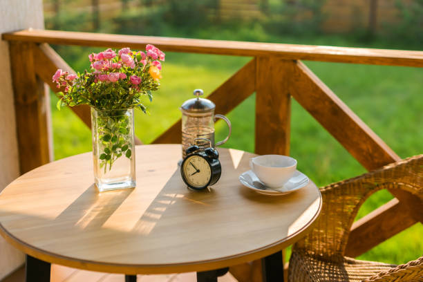 wooden table with a bouquet of flowers, an alarm clock and tea stands on a summer terrace. summer tea on terrace - garden decoration stock pictures, royalty-free photos & images