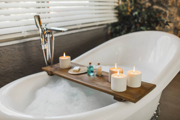 wooden tray on bath tub with burning candles, bath salt and shampoo in bottles, loofah sponge and soap - home decoration stock pictures, royalty-free photos & images