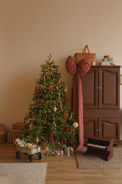 wrapped christmas gifts under an illuminated christmas tree and in a toy wagon in a living room with festive decorations - home decoration stock pictures, royalty-free photos & images