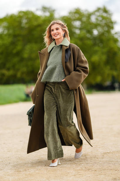 Xenia Adonts wears light green buttoned up long sleeve Loewe shirt, dark green Loewe sweater, dark green velvet Loewe pants, dark green Loewe coat,...