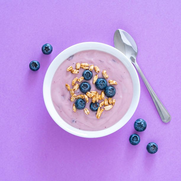 yogurt with berries and cereal on purple colored background. overhead view - food stock pictures, royalty-free photos & images