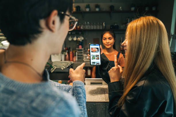 young adults browsing digital menu on mobile app while ordering at cafe - junk food stock pictures, royalty-free photos & images