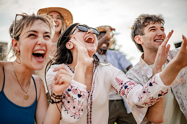 young adults celebrate joyfully at an outdoor music festival during sunset with lively dancing and excitement - concert stock pictures, royalty-free photos & images