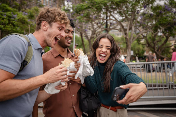young adults enjoying food and capturing joyful moments in sydney's vibrant outdoor scene - junk food stock pictures, royalty-free photos & images