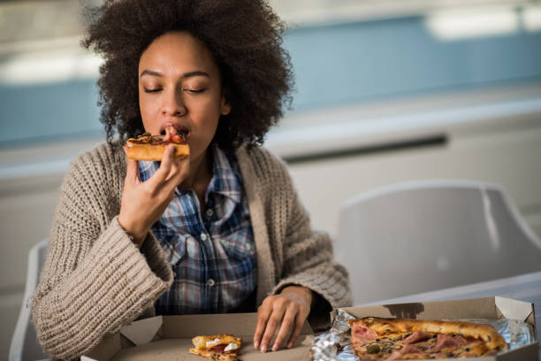 young african american woman eating pizza at home. - junk food stock pictures, royalty-free photos & images