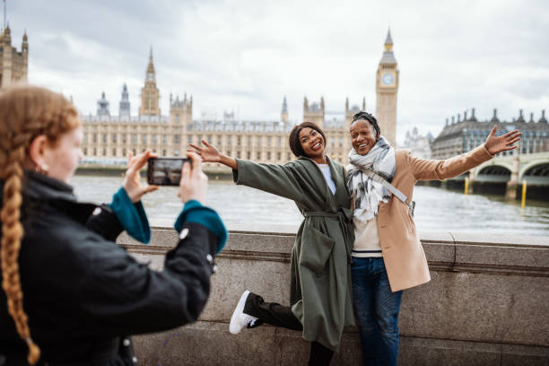 young african couple are tourist in london, in wintertime. redhead woman taking pictures with smart phone - travel stock pictures, royalty-free photos & images