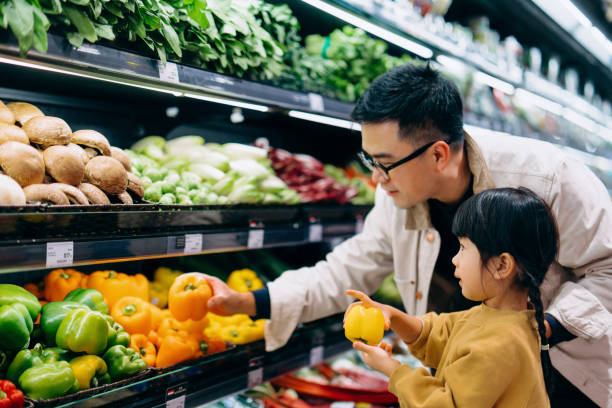 young asian father and her little daughter grocery shopping in supermarket. they are choosing fresh organic bell peppers together along the produce aisle. fruits and vegetables shopping. routine grocery shopping. going green 