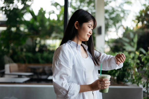 young asian female having matcha latte while checking time - junk food stock pictures, royalty-free photos & images