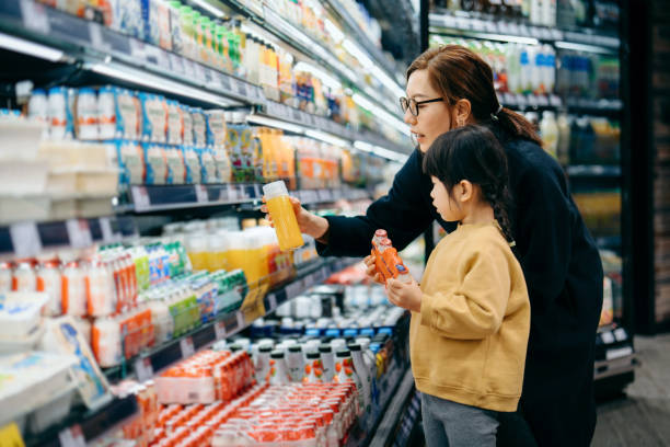 young asian mother and her little daughter grocery shopping in supermarket. they are choosing fresh fruit juice together along the beverage aisle. routine grocery shopping. healthy eating lifestyle - food stock pictures, roya