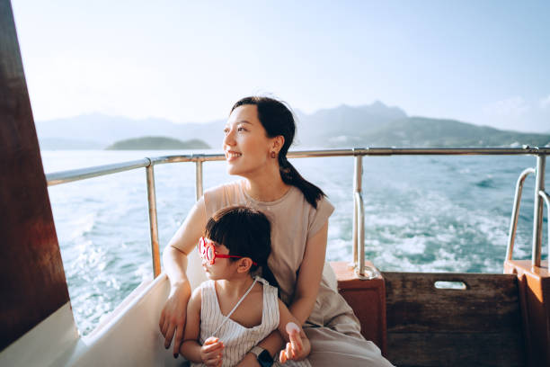 young asian mother and lovely little daughter with red sunglasses enjoying a yacht ride over nice calm sea on a summer day. looking over and relaxed at the sea. family lifestyle. enjoying outdoor fun, boat trip and sea vacati