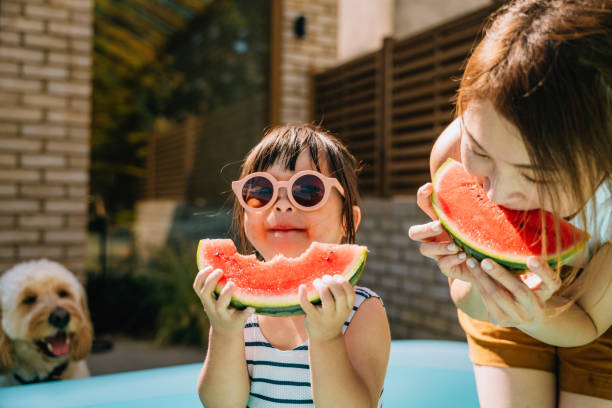 young asian toddler girl refreshing with watermelon slice with her mother in backyard - food stock pictures, royalty-free photos & images