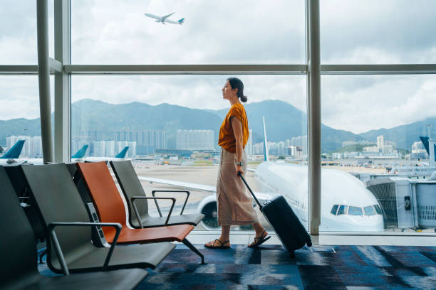 young asian woman carrying suitcase, walking by the window at airport terminal. young asian female traveller waiting for boarding at airport. business travel. travel and vacation concept - travel stock pictures, royalty-free 