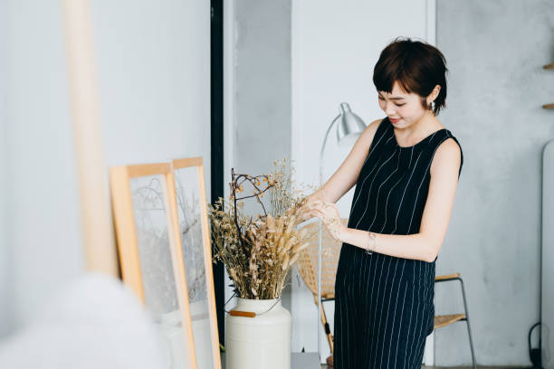 young asian woman decorating and arranging a vase with dried plants on cabinet in the living room at home - home decoration stock pictures, royalty-free photos & images