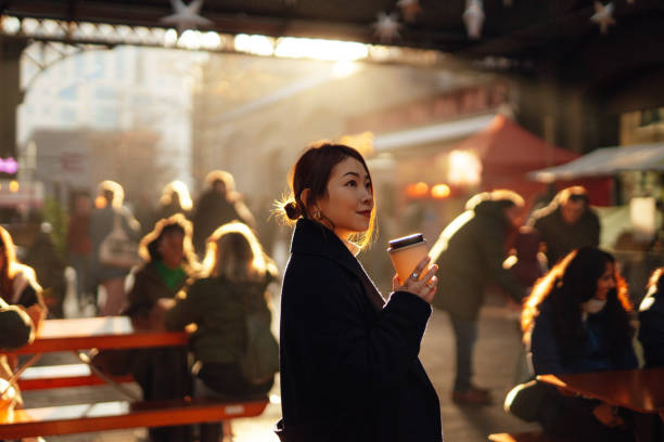 young asian woman drinking coffee at local street food market with moody sunlight - travel stock-fotos und bilder