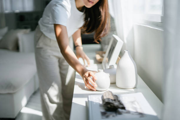 young asian woman enjoys her time at home, decorating and organising picture frames and vases on the shelf by the window - home decoration stock pictures, royalty-free photos & images