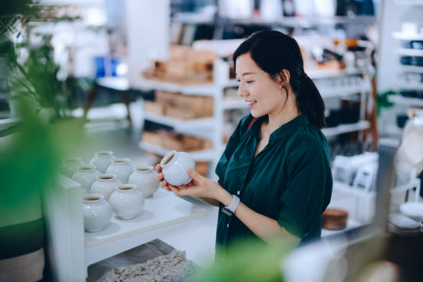young asian woman shopping for household necessities in a homeware store looking at a ceramic plant pot - home decoration stockfoto's en -beelden
