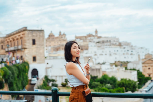 young asian woman using smart phone while overlooking the old town in ostuni, puglia, italy. - travel stockfoto's en -beelden