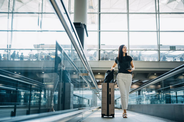 young asian woman with passport carrying suitcase walking in the airport concourse - travel stock pictures, royalty-free photos & images