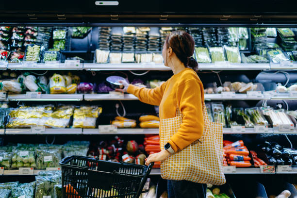 young asian woman with shopping cart, carrying a reusable shopping bag, shopping for fresh organic fruits and vegetables in supermarket. environmentally friendly concept. zero waste and plastic free. eco friendly shopping. su