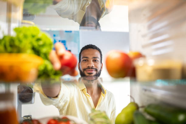 young black man grabbing food from his refrigerator - food stock pictures, royalty-free photos & images