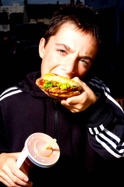 Young boy eating a fast food burger and holding a drink.