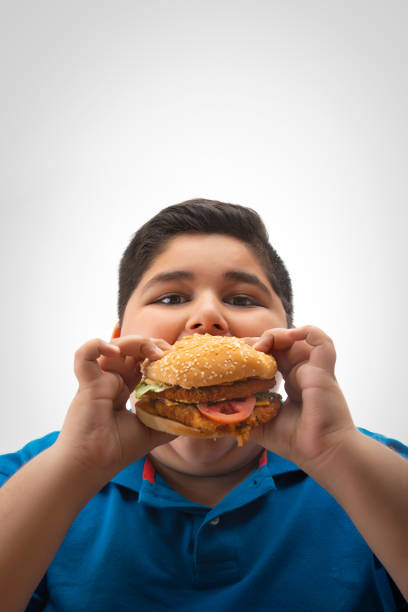 young boy eating a large burger in hand. (obesity) - junk food stock pictures, royalty-free photos & images