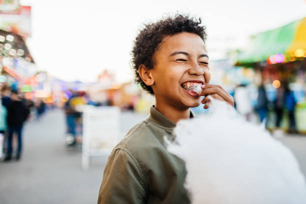 young boy with braces eating candy floss at fair - food stock pictures, royalty-free photos & images