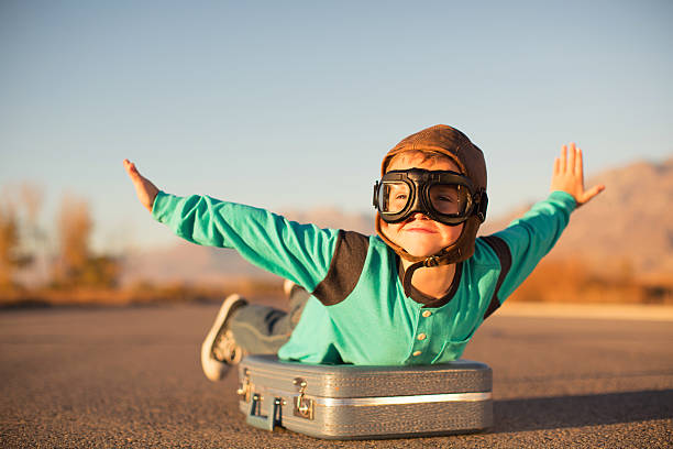 young boy with goggles imagines flying on suitcase - travel stock pictures, royalty-free photos & images