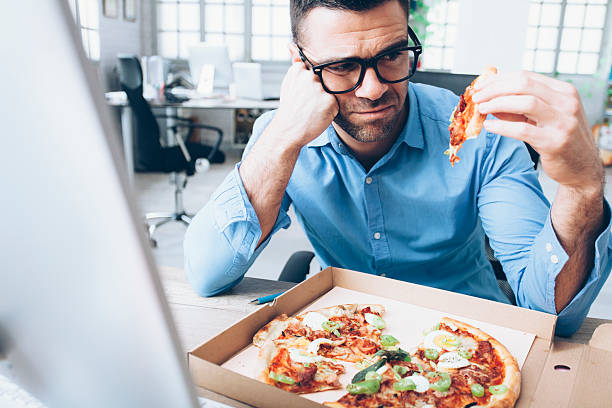 young businessman having unpleasent pizza lunch break at workplace - junk food stock pictures, royalty-free photos & images