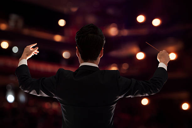 young conductor with baton raised at a performance, rear view - concert stock pictures, royalty-free photos & images