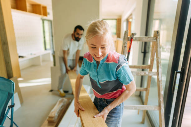young couple carrying a plank together during their moving into a new house - home decoration stock pictures, royalty-free photos & images