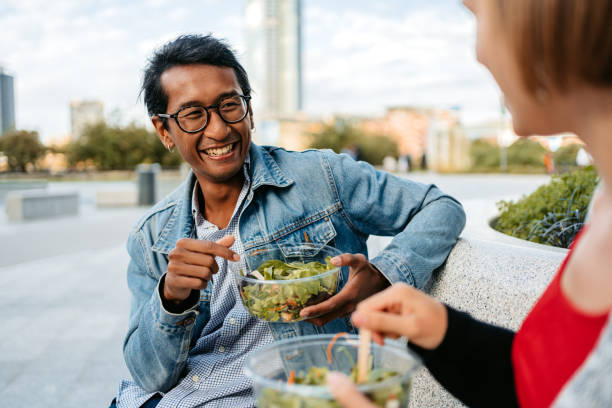 young couple eating a salad and talking on the bench in milan - junk food stock pictures, royalty-free photos & images