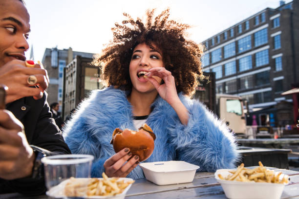 young couple eating burger and chips outdoors - junk food stock pictures, royalty-free photos & images