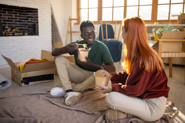young couple eating noodles in their new apartment - junk food stock pictures, royalty-free photos & images