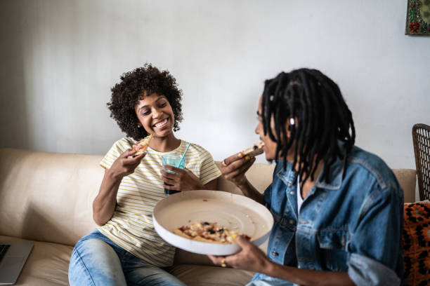 young couple eating pizza together at home - junk food stock pictures, royalty-free photos & images