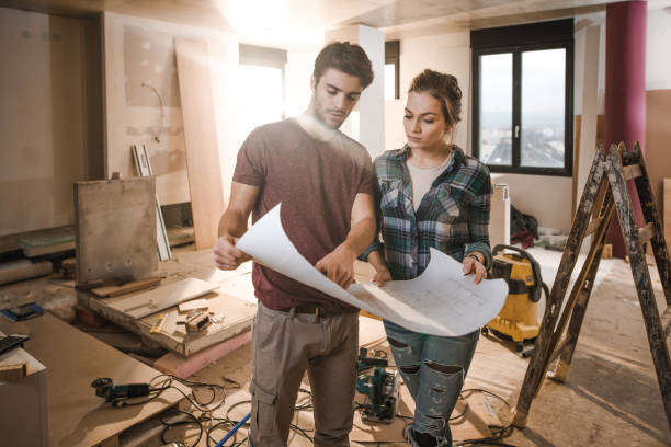 young couple examining blueprints while being on construction site in their apartment. - home decoration stock pictures, royalty-free photos & images