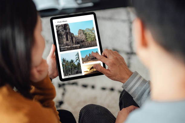 young couple looking at photo album on digital tablet - travel stock-fotos und bilder