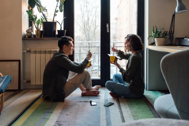 young couple with take out food siting by window at home - junk food stock pictures, royalty-free photos & images
