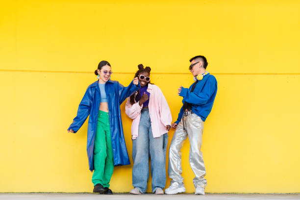 young friends dancing energetically, wearing trendy outfits against bright yellow backdrop, expressing vibrant youthful style - fashion stock pictures, royalty-free photos & images
