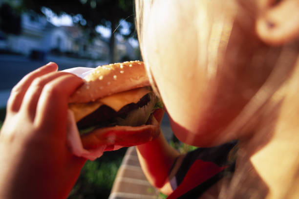 young girl eating a hamburger - junk food stock pictures, royalty-free photos & images