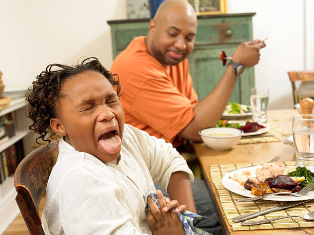 young girl sits at a table for lunch with her father, sticking out her tongue in disgust at the food - food stock pictures, royalty-free photos & images