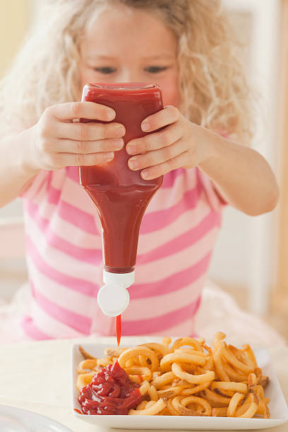 young girl squeezing ketchup on french fries - junk food stockfoto's en -beelden