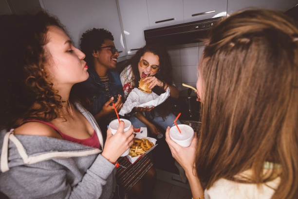 young girls having fun eating fast food at house party - junk food stock pictures, royalty-free photos & images
