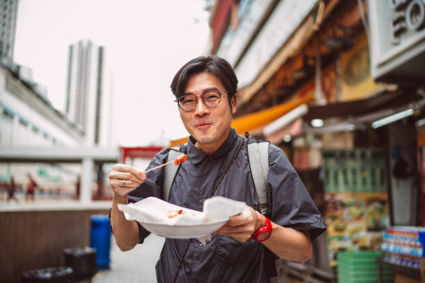 young handsome man enjoying hong kong local street food joyfully in street - food stock pictures, royalty-free photos & images