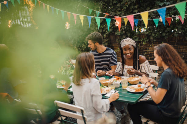 young male and female friends enjoying food at table during dinner party in backyard - garden decoration stock pictures, royalty-free photos & images